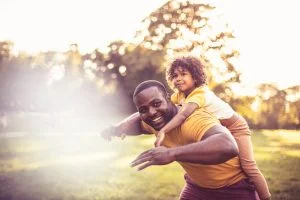 Father carrying daughter piggyback. African American father and daughter having fun outdoors.